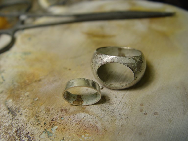Zwei unvollendete Silberringe auf einem Werkstück mit Werkzeugen im Hintergrund.